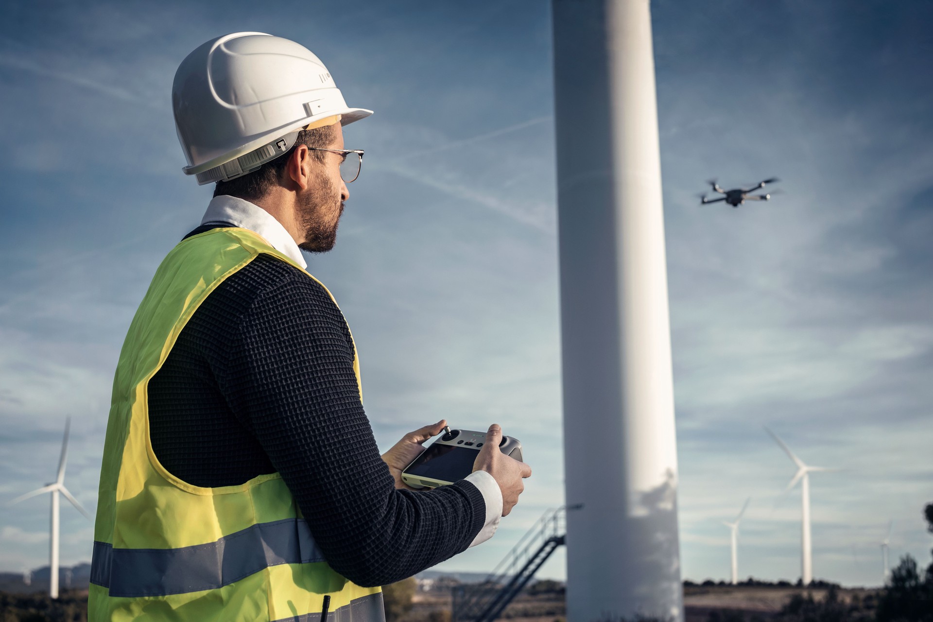 Mature man engineers flying a drone over the wind generator field while checking that everything is correct