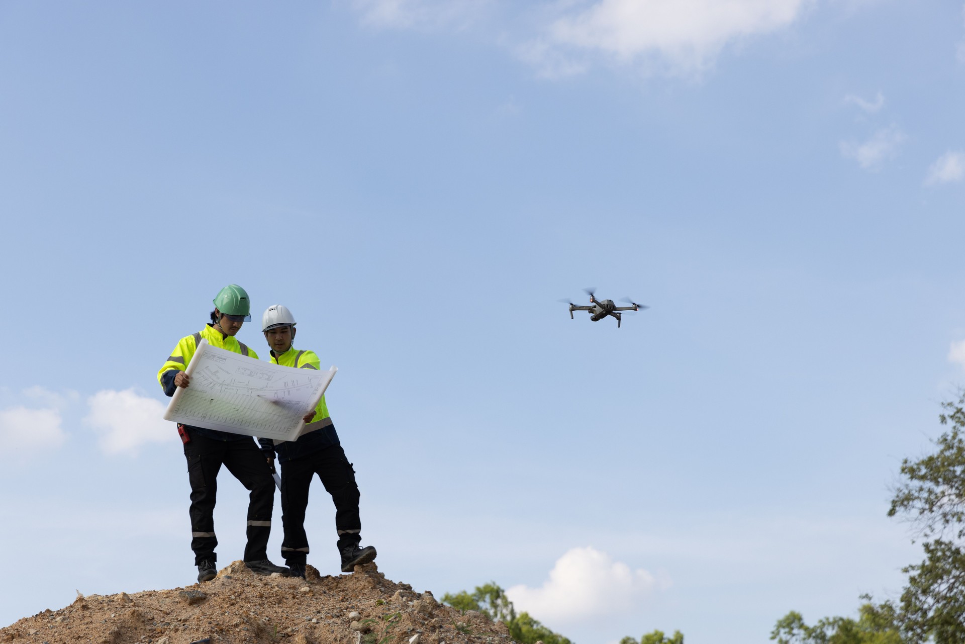 Two male civil engineers stand on a high pile of dirt to survey the area, laying the drainage system with aerial photography equipment as an aid in surveying.